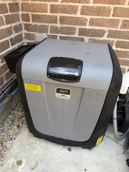 Pool heater installed on a concrete pad against a brick wall