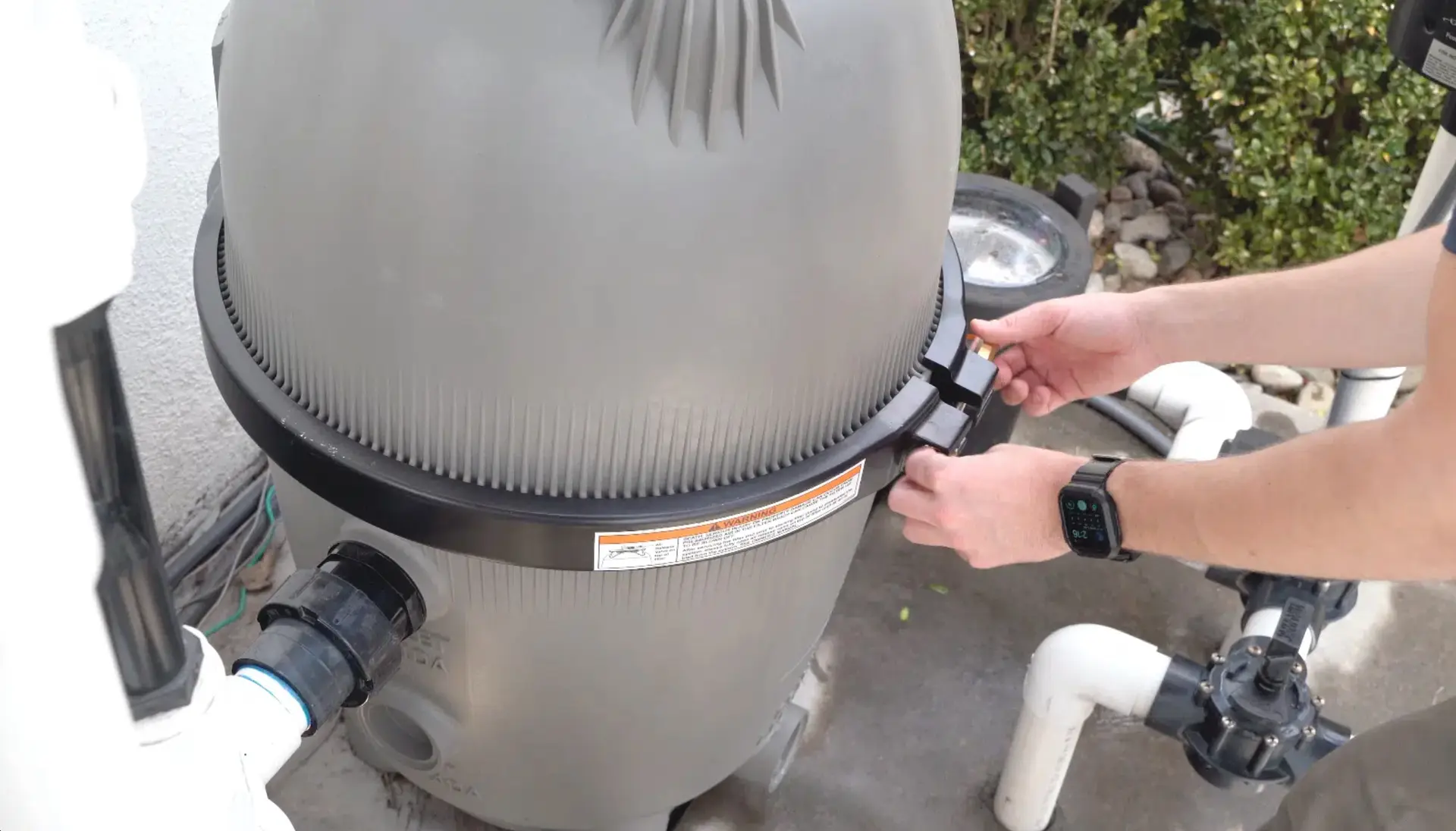 Hands opening a cartridge pool filter housing for cleaning