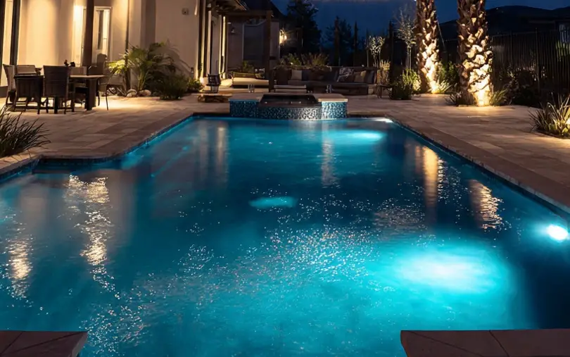 Backyard pool with underwater lighting and palm trees at night
