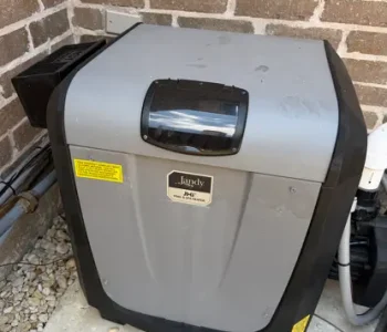 Pool heater installed on a concrete pad against a brick wall